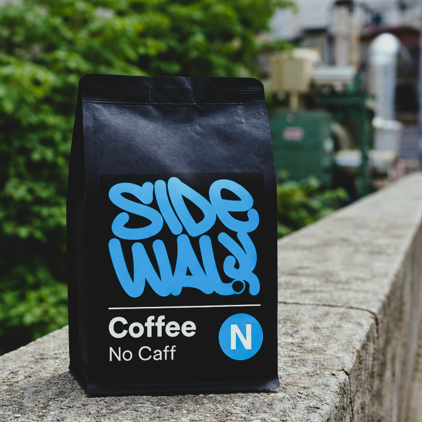 Black coffee bag with blue text on a stone surface, blurred greenery in the background