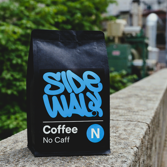 Black coffee bag with blue text on a stone surface, blurred greenery in the background
